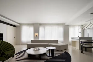 A modern living room with a minimalist design, featuring a white sofa, round coffee tables, and a geometric rug. Large window