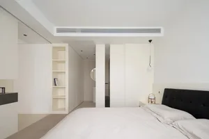A minimalist bedroom with a white bed, white cabinets, and a black headboard.