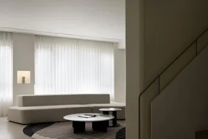 Minimalist living room with white furniture, floor-to-ceiling windows, and a striped rug.