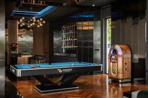 A modern minimalist living room featuring a wooden floor and glass walls, with a pool table and jukebox.