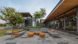 A modern residential exterior with dark grey walls, wooden accents, and a combination of trees and foliage.
