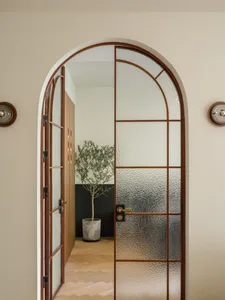 A view of a modern architectural entryway featuring an arched glass door, wooden flooring, and a potted plant in the backgrou