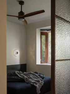 Minimalist bedroom featuring a bed with a grey blanket, dark wood headboard, and a side light fixture on the wall.