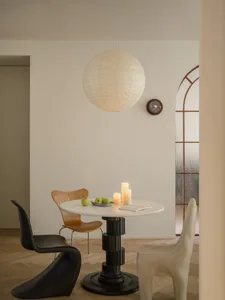 Circular table with minimalist design, featuring wooden chairs, pendant light, and green apples on a white table.