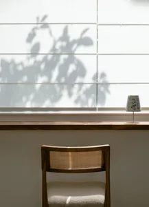 A minimalist interior with a wooden chair and fabric seating, featuring a shadow of greenery on the window.