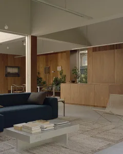 A minimalist living room with wooden walls, blue couch, and white coffee table.
