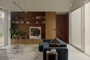 A modern industrial living room featuring a dark wooden shelf, blue sofa, and potted plants on a white rug.