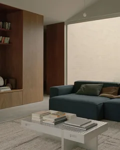A modern living room featuring a blue sectional sofa, a white perforated coffee table with stacks of books, and a wooden shel
