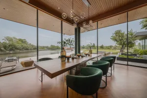 A modern living room with wooden flooring, green chairs, and a large glass window showing a view of a river.