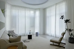 A minimalist living room with white curtains, textured cushions, and a cozy atmosphere.