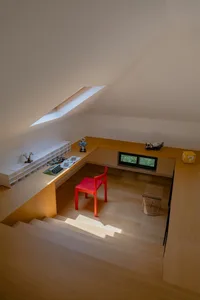 An image of a modern office space featuring a wooden desk and a red chair with a skylight above.