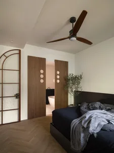 A modern bedroom featuring a black bed with a dark-colored headboard and wooden floors, with a glimpse of a bathroom in the b