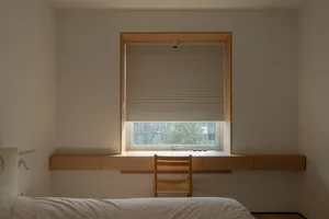 簡約臥室內設有懸浮式書桌與木椅，搭配淺色牆面及百葉窗。