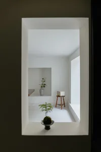 Modern minimalist room with concrete walls and floor, featuring a small plant and a simple wooden stool.