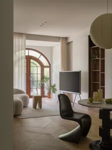 A modern living room featuring wooden flooring, a black curved chair, a round table with green apples, and a curved door with