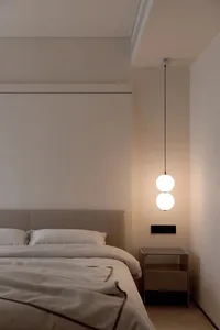 Modern minimalist bedroom with beige walls, white headboard, and textured blanket on the bed.
