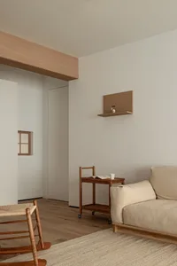 Modern minimalist living room featuring a comfortable beige sofa, wooden chairs, and a small wooden side table with a book an