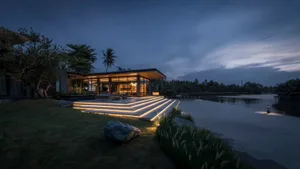 Nighttime photograph of a modern house featuring wooden elements and glass walls located near a waterfront.