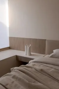 A minimalist bedroom featuring a bed with a wood headboard and beige bedding.