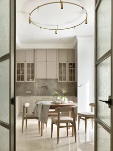 A minimalist residential kitchen with white cabinets, marble countertops, and a round dining table.