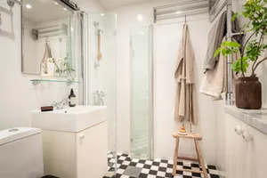 A minimalist bathroom with white tiled flooring, glass shower enclosure, and furniture.