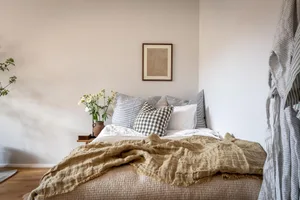 A minimalist bedroom featuring neutral textiles, a cozy armchair, and a warm wooden floor.