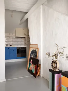 A modern kitchen with white painted walls, blue cabinets, and framed artwork leaning against the wall.