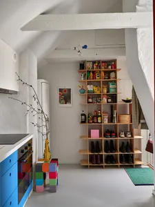 A minimalist kitchen features a tall wooden shelf stocked with various food and kitchen items, a colorful block storage unit,
