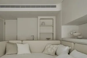 A minimalist living room with a white fabric couch, white cushions, and a white wall shelf.