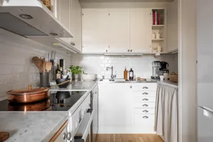 A minimalist kitchen with white tiled walls, wooden cabinets, and a small round dining table with two chairs.