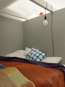 A modern bedroom with a bed featuring a blue and white checkered pillow and an orange and blue patterned blanket.