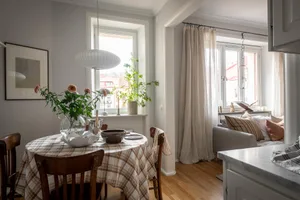 A modern kitchen with a round table covered in a plaid tablecloth, wooden chairs, and a glass vase with flowers.