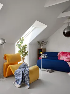 A minimalist living room with a yellow curved chair, blue sofa, and a skylight in the ceiling.
