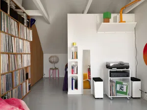 A minimalist living room with white floor, walls, and ceiling, featuring white glass shelving units, a yellow chair, and a co