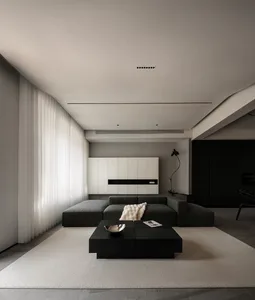 A minimalist living room with a fabric sofa, black coffee table, and white curtains.
