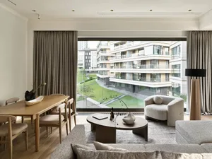 Light-filled apartment featuring modern furniture and wooden accents, overlooking adjacent apartment buildings.