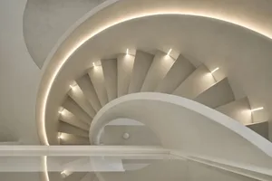 Circular modern staircase with concrete steps, illuminated by warm lighting fixtures.
