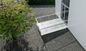 Modern exterior space featuring a concrete terrace with glass railings and gravel path.