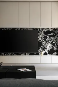 A modern minimalist living room featuring a large black flat-screen TV mounted on a black and white marble wall with a white 
