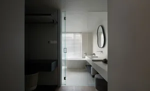 Modern minimalist bathroom with a freestanding glass shower enclosure, white porcelain sink, and a large window with white bl