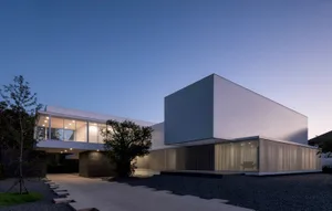 A modern residential building with glass walls, concrete exterior, and metallic elements.