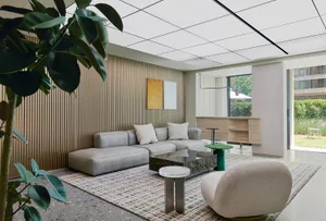 A minimalist living room with concrete and glass elements, featuring a modern sofa, coffee table, and a green stool.