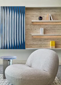 A minimalist living room with a gray upholstered chair, a transparent side table, and a blue and white abstract painting on a