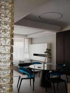 Modern living room featuring transparent blue chairs, glass table, and black accents.