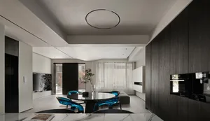 A modern living-dining room with mixed materials, featuring sleek black furniture, teal chairs, and a round table.