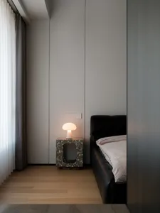 Modern minimalist bedroom with a terrazzo side table featuring a mushroom-shaped lamp and a black upholstered bed with a pink