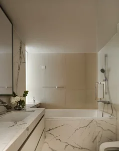 Modern minimalist bathroom with white marble vanity and tub, glass shower enclosure, and beige tiled walls.
