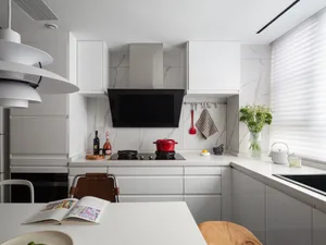 Modern minimalist kitchen with white marble countertops and stainless steel appliances, featuring a white pendant light fixtu