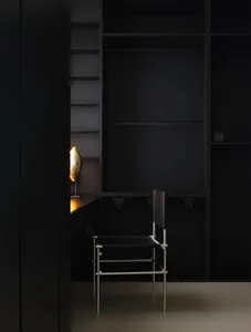 A minimalist wardrobe with black metal frame and shelves, illuminated by a golden lamp.