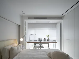 A minimalist white bedroom with a bed, a desk, and a small office space.